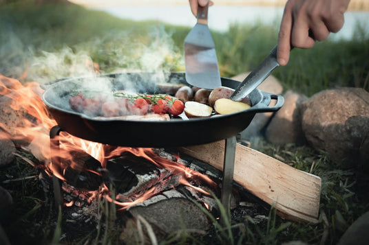 Person grillt Gemüse auf einer Feuerpfanne über dem Lagerfeuer