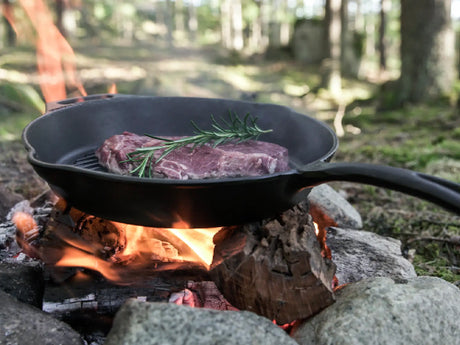 Fleisch in einer gusseisernen Pfanne über dem Lagerfeuer