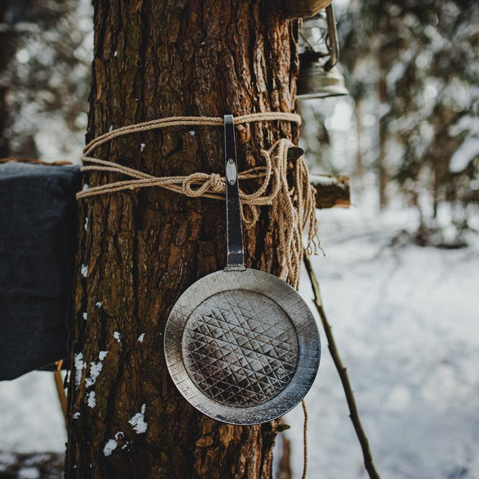 Schmiedeeiserne Pfanne aufgehängt an einem Baum im winterlichen Umfeld